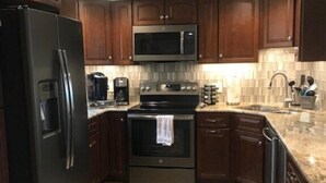 A kitchen with dark wooden cabinets, a stainless steel refrigerator, a microwave, an oven, and a dishwasher. - Summerhouse 101:  Luxury Condo on Beach (St. Augustine)