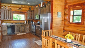 A wooden cabin interior with a kitchen, dining area, and large windows.