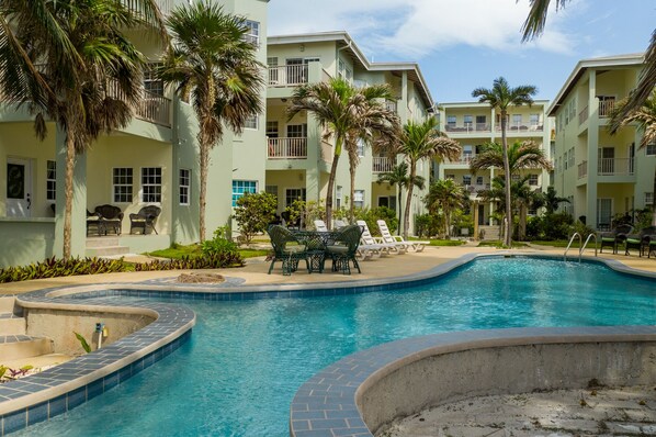 A pool area with lounge chairs and palm trees, surrounded by multi-story buildings with balconies. - Incredible Views from this 2 bedroom Ocean View Condo - Gold Standard Approved (San Pedro)