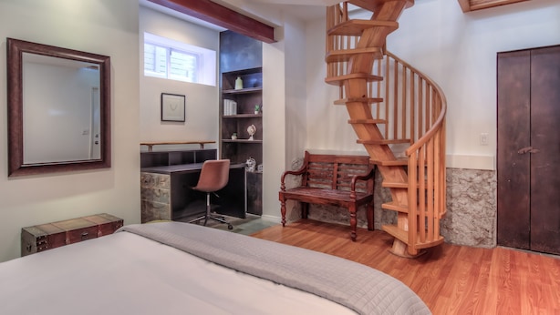 Quarto com escada em espiral de madeira, uma mesa com cadeira, cama e guarda-roupa.