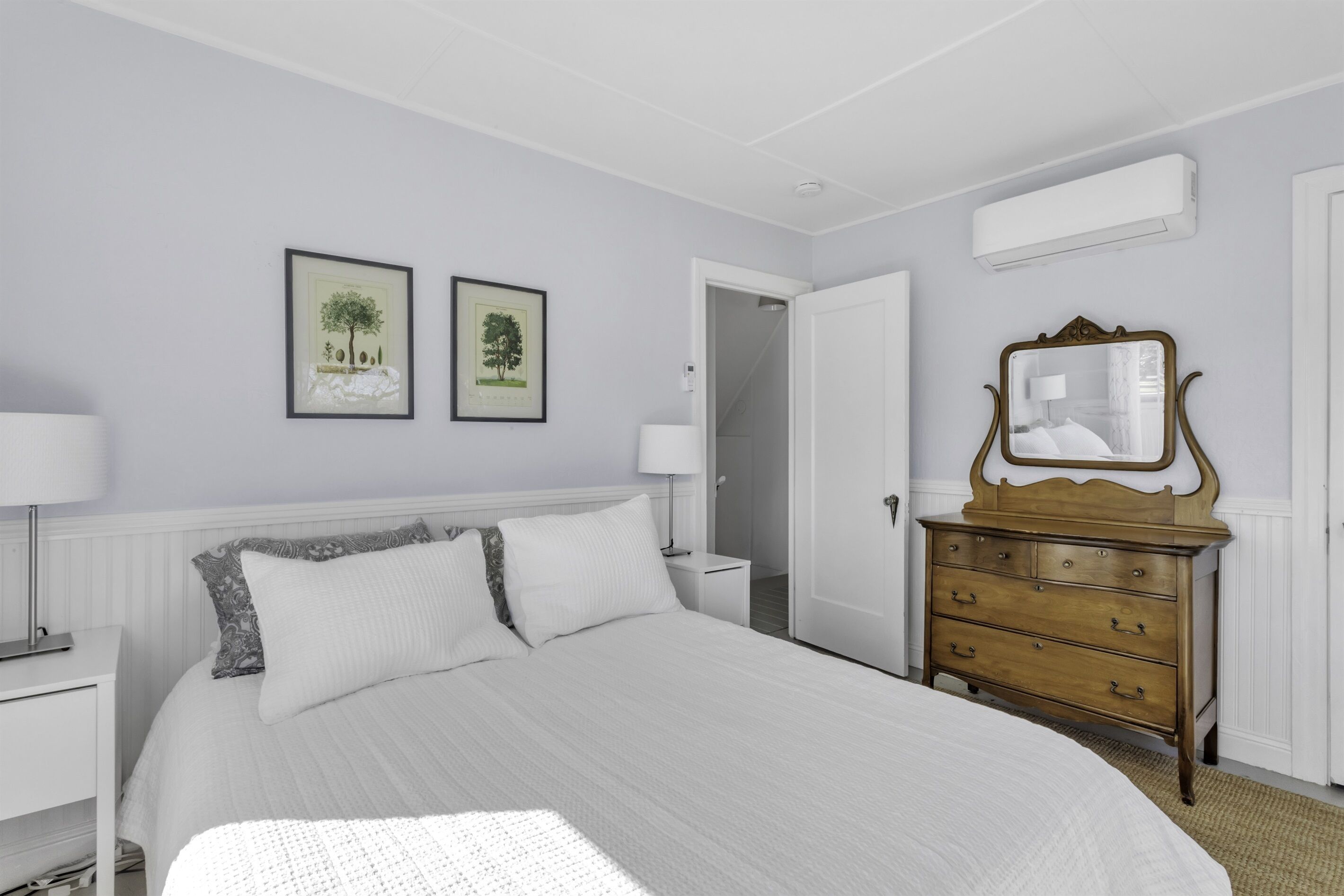 Une chambre à coucher avec un lit, deux tableaux encadrés, une commode et un miroir.