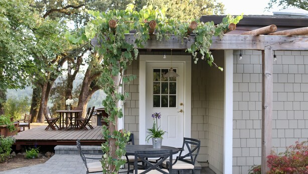 An outdoor patio with a wooden deck, a table with chairs, and a door with a hanging light fixture. - Wine Country Farmhouse with Hot Tub (Santa Rosa)