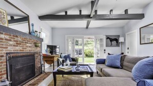 A living room with a fireplace, a sofa, a coffee table, and a large window with a view of the outdoors. - Wine Country Farmhouse with Hot Tub (Santa Rosa)