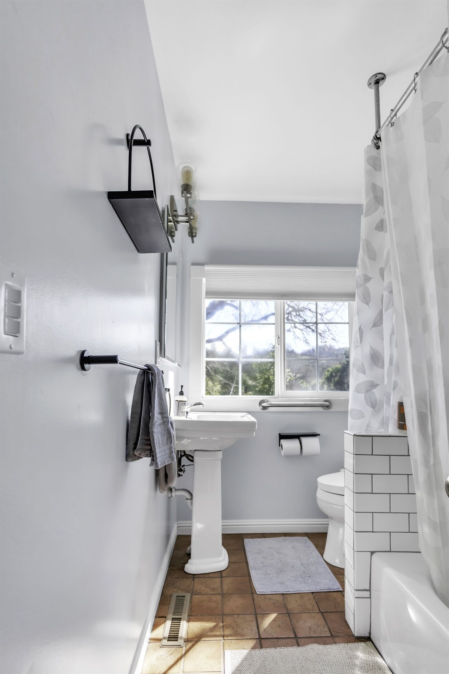 Een badkamer met een wit wastafelmeubel, toilet en badkuip. Er is een raam dat voor daglicht zorgt, en een handdoekhouder is zichtbaar.