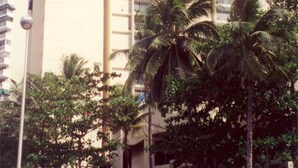 Un hotel con un llamativo letrero 'esj', rodeado de palmeras y una zona de arena con sillones de descanso.
