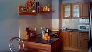 A kitchen with wooden cabinets, a microwave, a kettle, and a fruit bowl with oranges on the counter. - Greek Rooms in the City Center (Sofia)