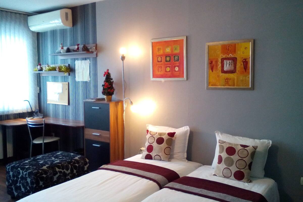 A hotel room with two beds, a desk, a chair, and a small Christmas tree.