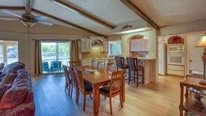 A spacious dining area with a large wooden table and chairs, a ceiling fan, and a view of the outdoors through large windows.