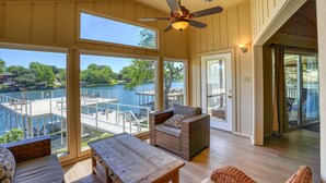 A spacious room with large windows overlooking a dock and water, a ceiling fan, and a wooden table.