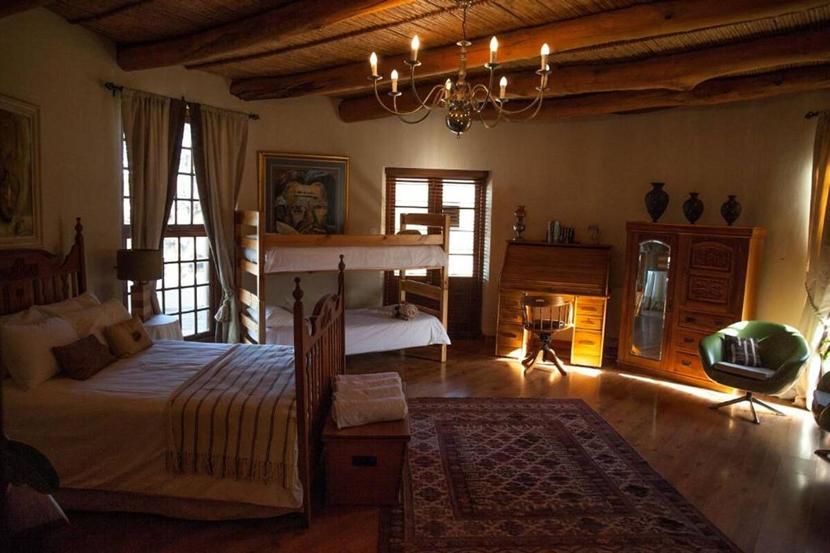 Una habitación con techo de madera, un candelabro, una cama con manta a rayas, una silla y un aparador.