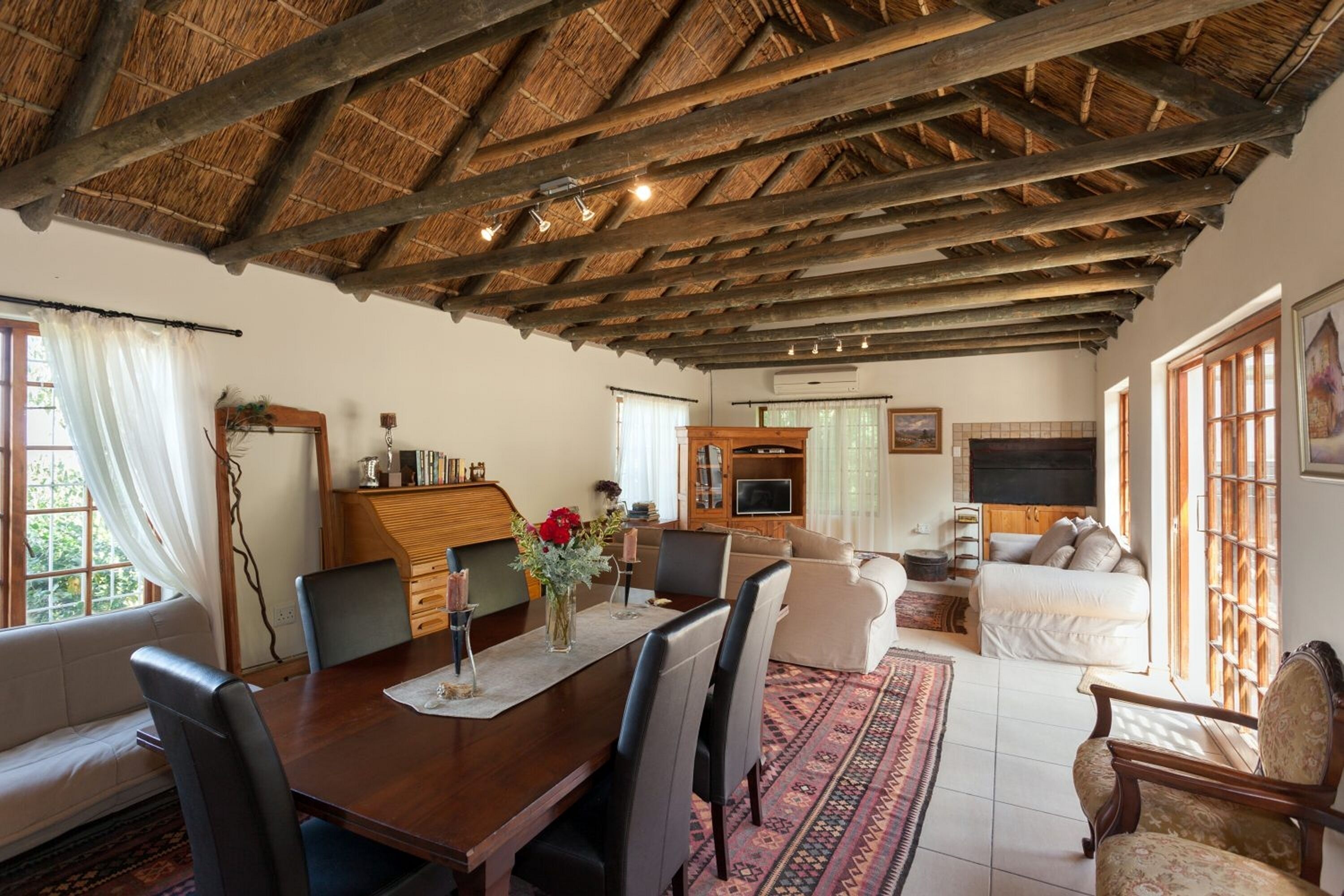 A spacious living area with a wooden ceiling, a dining table with chairs, a sofa, and a television.