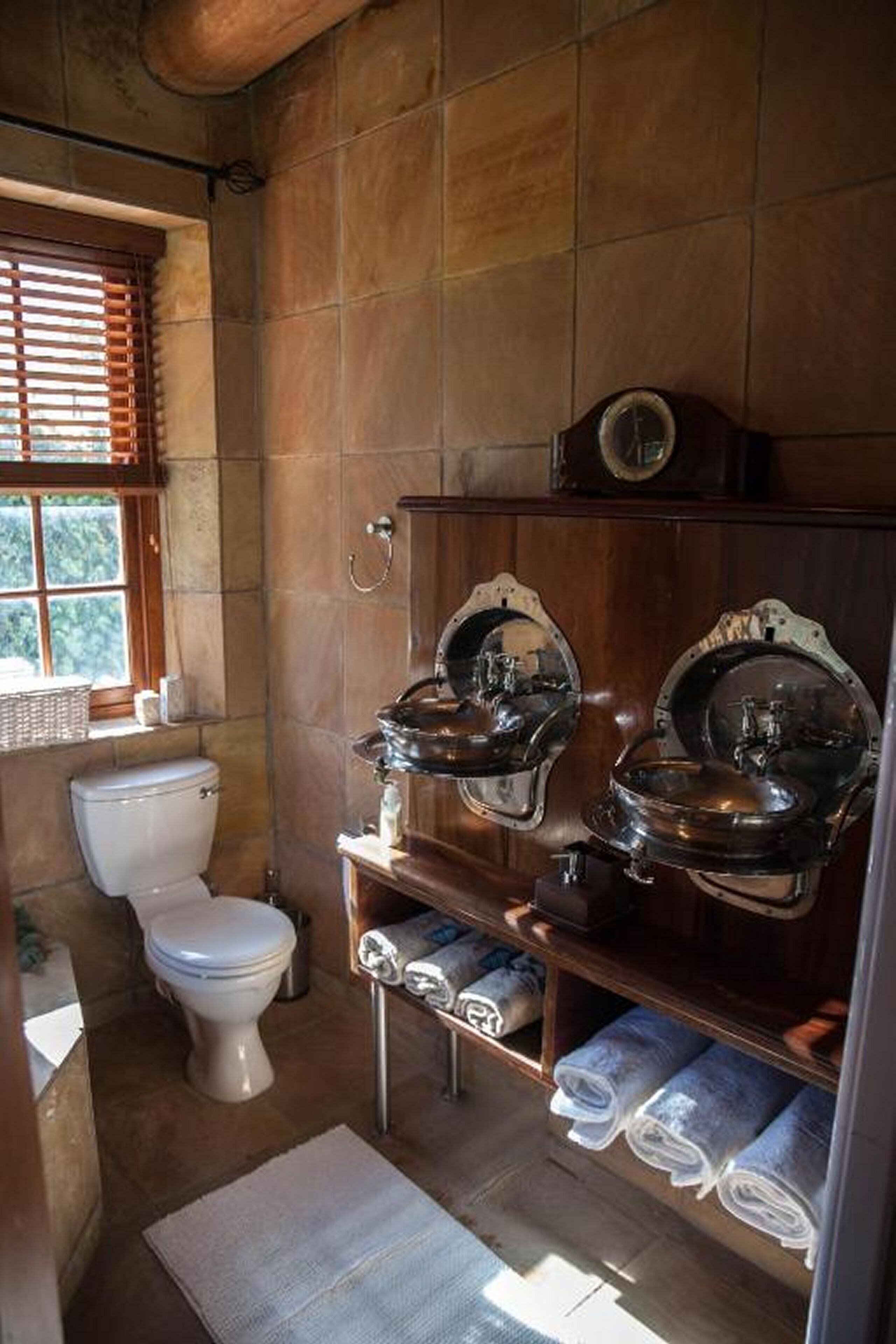 Un baño con inodoro, dos lavamanos y toallas en repisas.