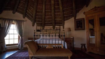 A bedroom with a four-poster bed, a wooden bench, a wooden cabinet, and a large window with curtains.