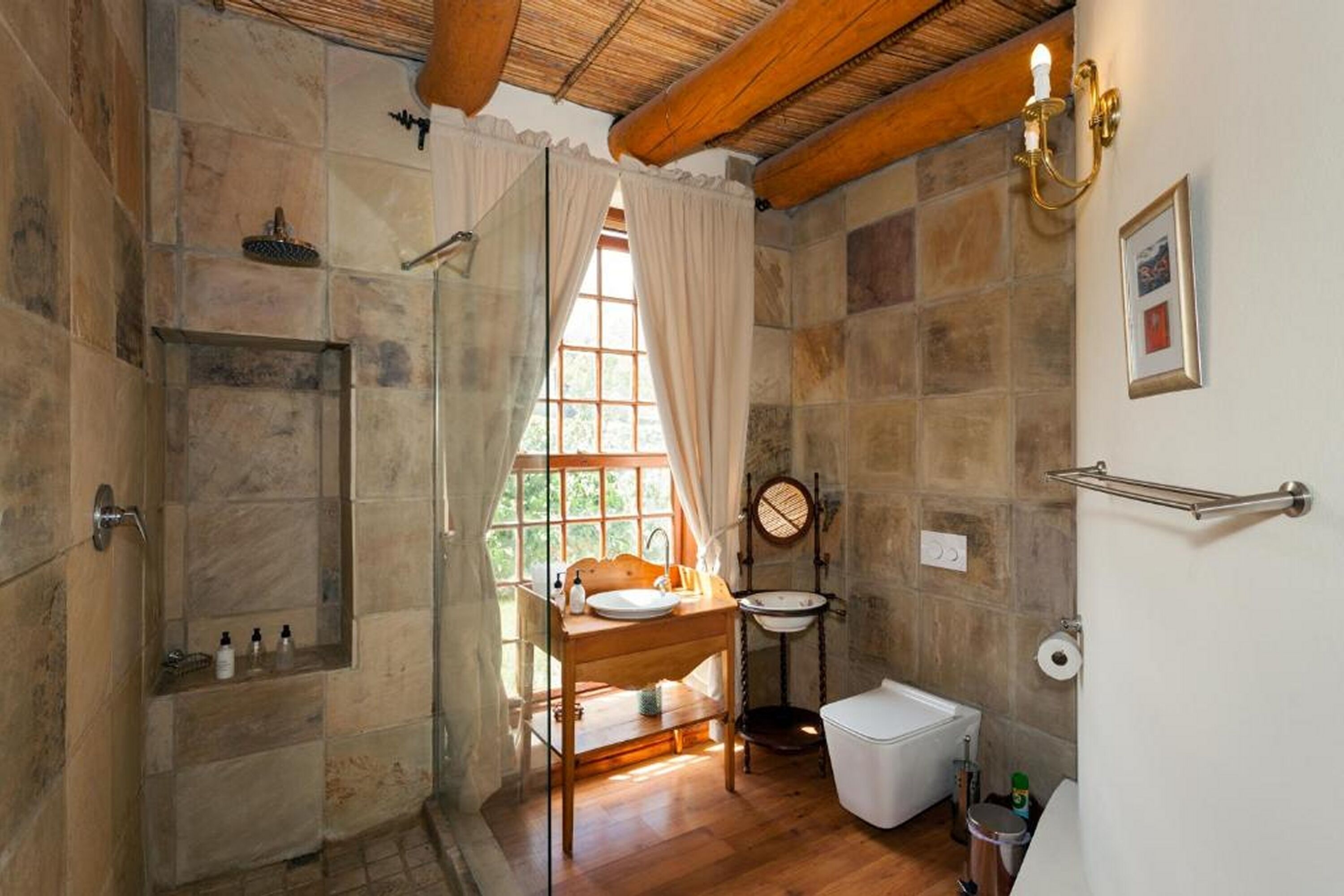 Een badkamer met een douche, een wastafel, een toilet en een raam met gordijnen.
