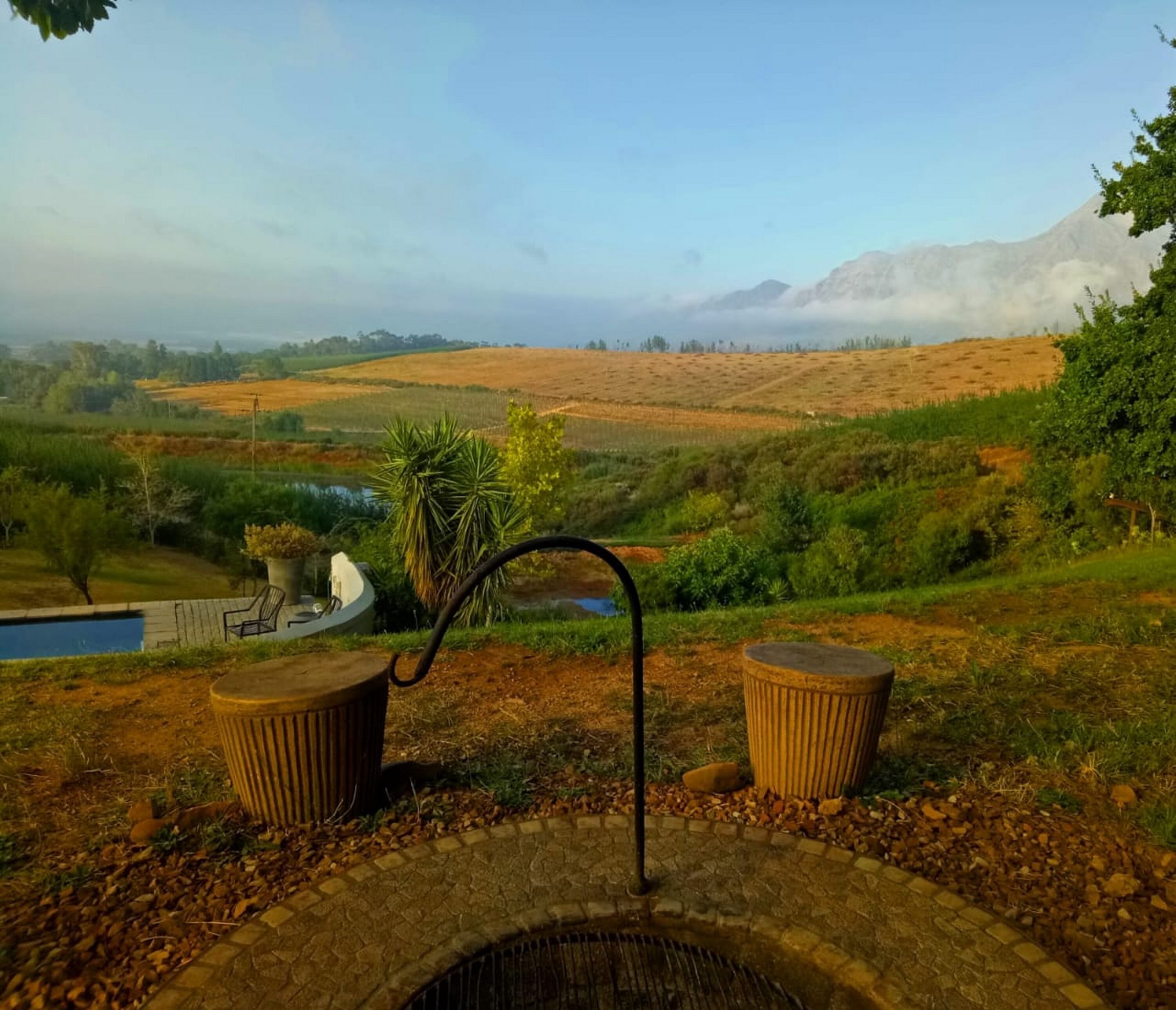 A patio with a fire pit, two trash bins, and a view of a hilly landscape with a body of water and trees.