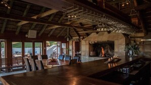 A spacious dining area with a long wooden table and chairs, a stone fireplace, and a view of the outdoors. - Tulbagh Mountain Manor (Tulbagh)
