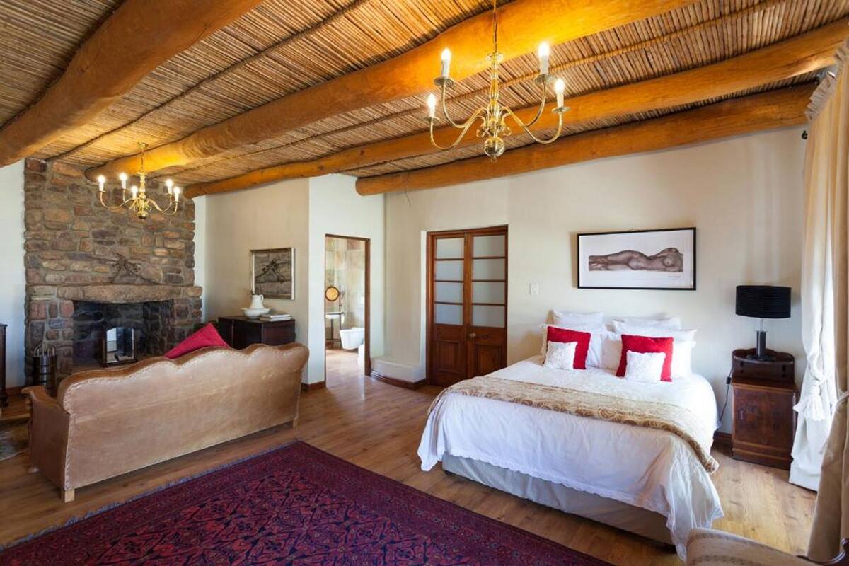 Un dormitorio espacioso con una cama grande, un sofá más pequeño, una chimenea de piedra y un candelabro.