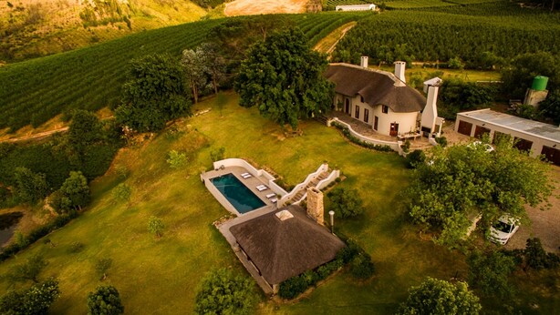 An aerial view of a property with a swimming pool, a large house with a thatched roof, and surrounding vineyards. - Tulbagh Mountain Manor (Tulbagh)