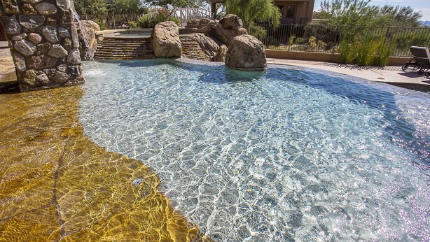 A clear pool with rocks, a stone wall, and a fenced area with a chair. - Private with Mountain Views and City Lights (Scottsdale)