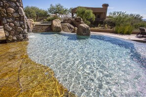 A clear pool with rocks, a stone wall, and a fenced area with a chair. - Private with Mountain Views and City Lights (Scottsdale)