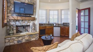 A living room with a stone fireplace, a flat-screen TV, a dining area with wooden cabinets, and a kitchen with a microwave. - Private with Mountain Views and City Lights (Scottsdale)