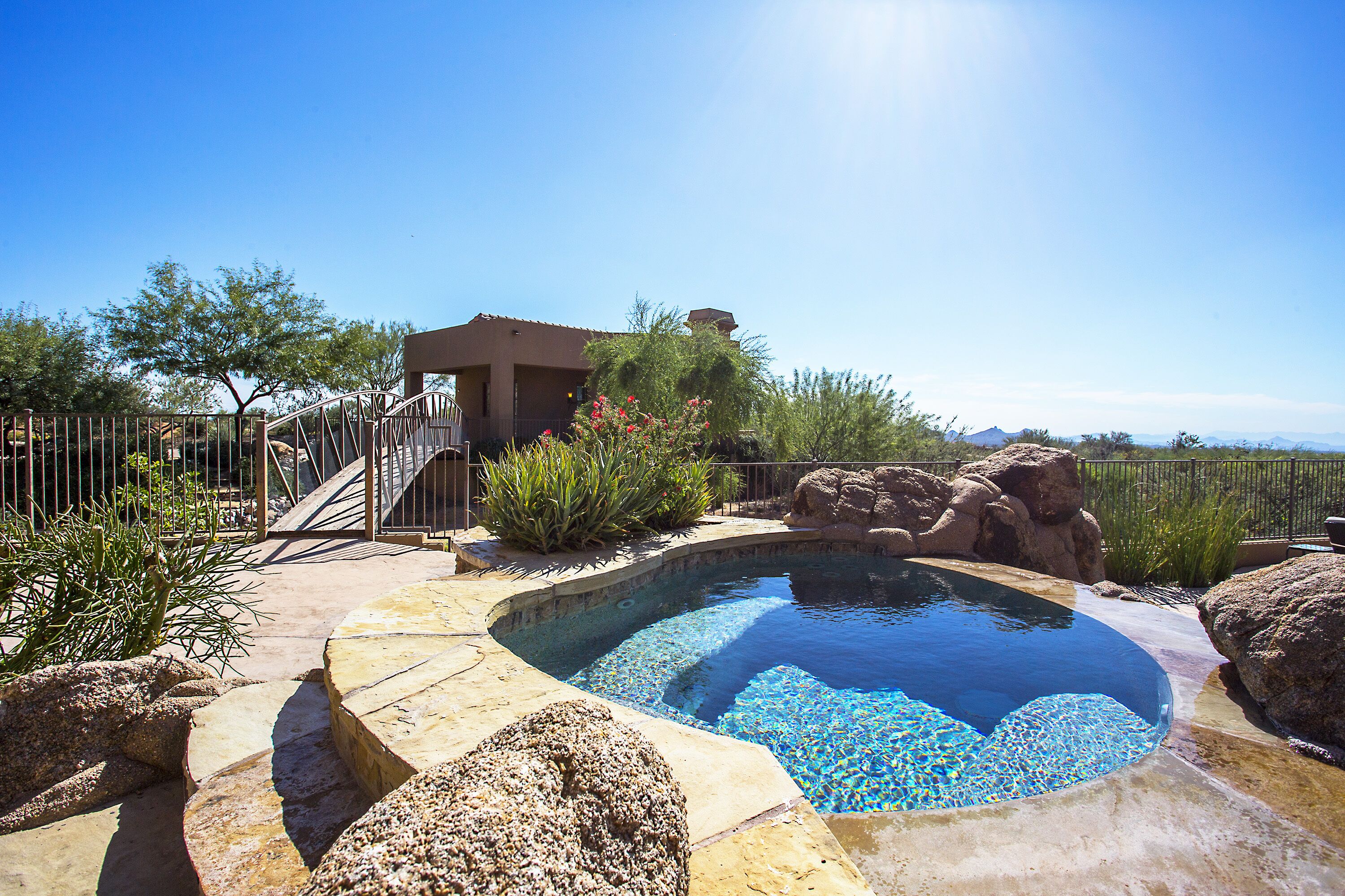A swimming pool with a stone border, surrounded by rocks and plants, and a small building with a balcony.