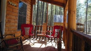 Uma cabana de madeira com varanda, com duas cadeiras dobráveis vermelhas e uma pequena mesa.