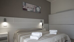 A neatly made bed with striped bedding and two white bedside tables, one with a lamp. - Hotel San Domenico (Cervia)