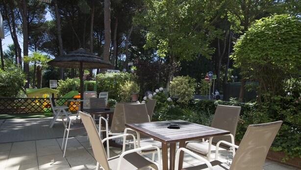 An outdoor patio area with a wooden table and chairs, surrounded by greenery and trees. - Hotel San Domenico (Cervia)