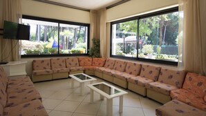 A living room with a large sectional sofa, two glass-top coffee tables, and a flat-screen TV mounted on the wall. - Hotel San Domenico (Cervia)