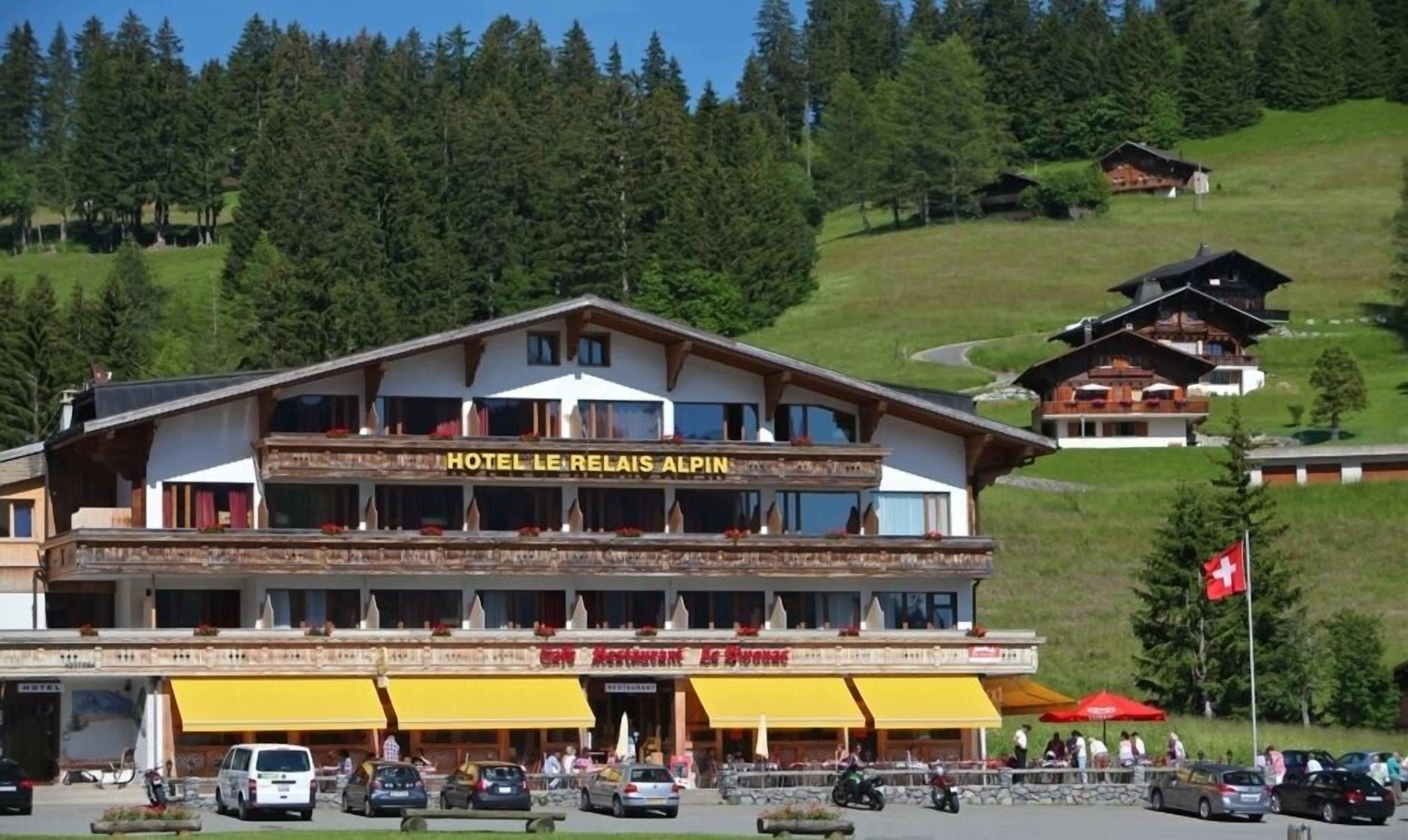 A hotel with a restaurant named "Le Relais Alpina" on the ground floor, featuring a traditional Alpine architectural style with wooden balconies and large windows.