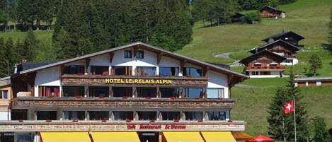 A hotel with a restaurant named "Le Relais Alpina" on the ground floor, featuring a traditional Alpine architectural style with wooden balconies and large windows.