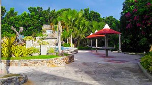 A stone pathway leading to a gazebo with a red roof, surrounded by lush greenery and a small fountain. - Punta Aguila Resort & Hotel (San Juan)