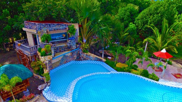 A large outdoor swimming pool with a stone structure and a sign indicating a hotel. - Punta Aguila Resort & Hotel (San Juan)