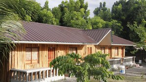 A wooden cabin with a metal roof, a porch, and a gravel driveway. - Punta Aguila Resort & Hotel (San Juan)