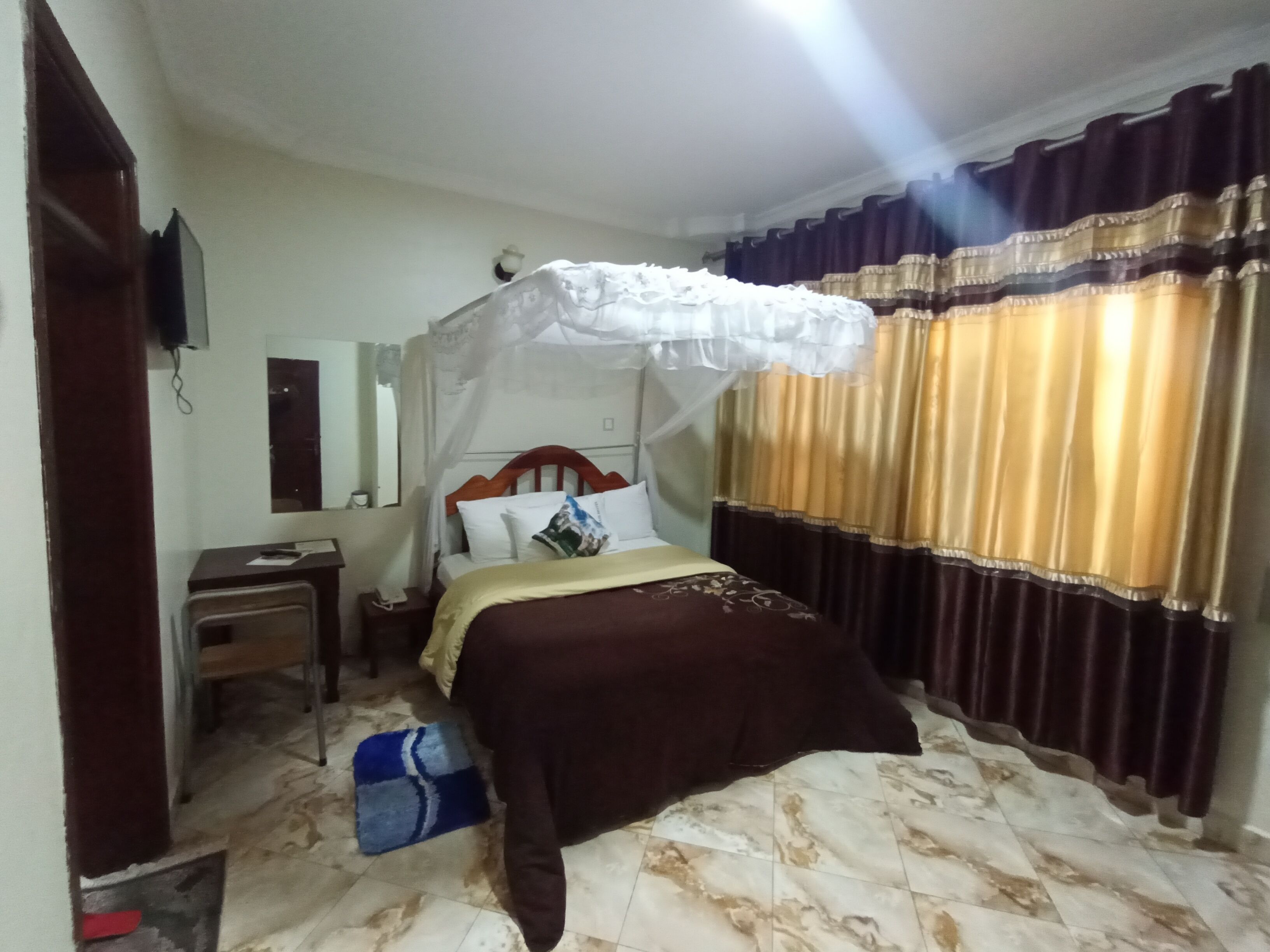 A bedroom with a bed, a desk, a chair, a mirror, and curtains.
