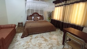 Un dormitorio con cama, una silla, una mesita, un jarrón decorativo y una ventana con cortinas.