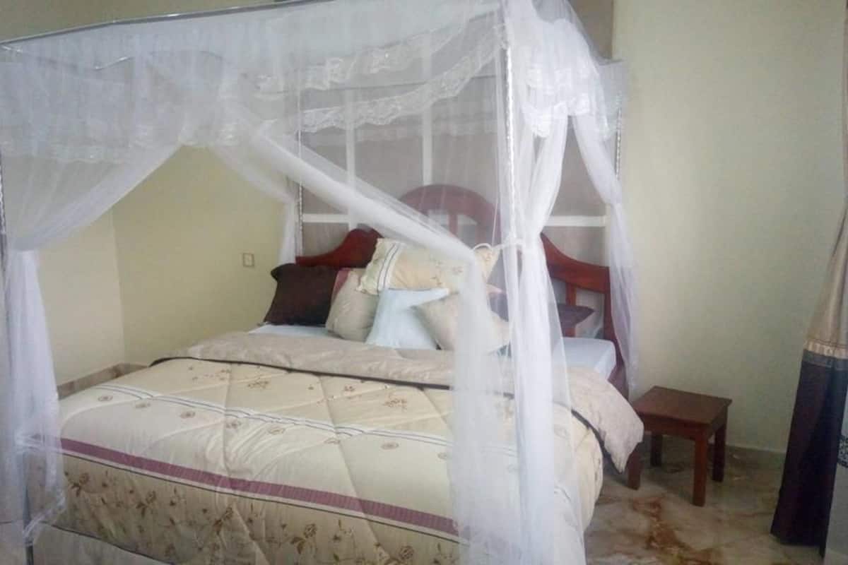 A bed with a canopy, a wooden nightstand, and a chair in a room with plain walls and a tiled floor.