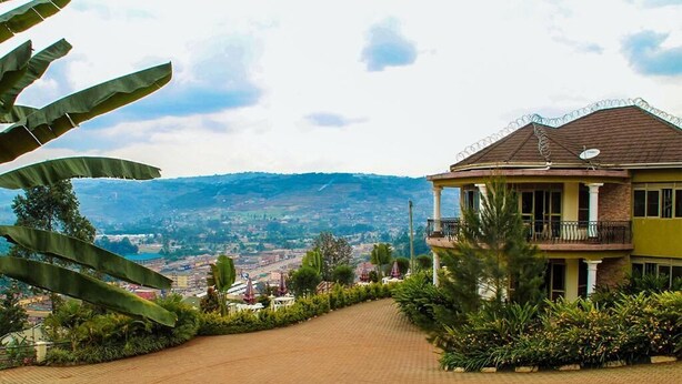 Una casa con entrada pavimentada que conduce a un balcón, rodeada de vegetación y con vistas a un paisaje montañoso.