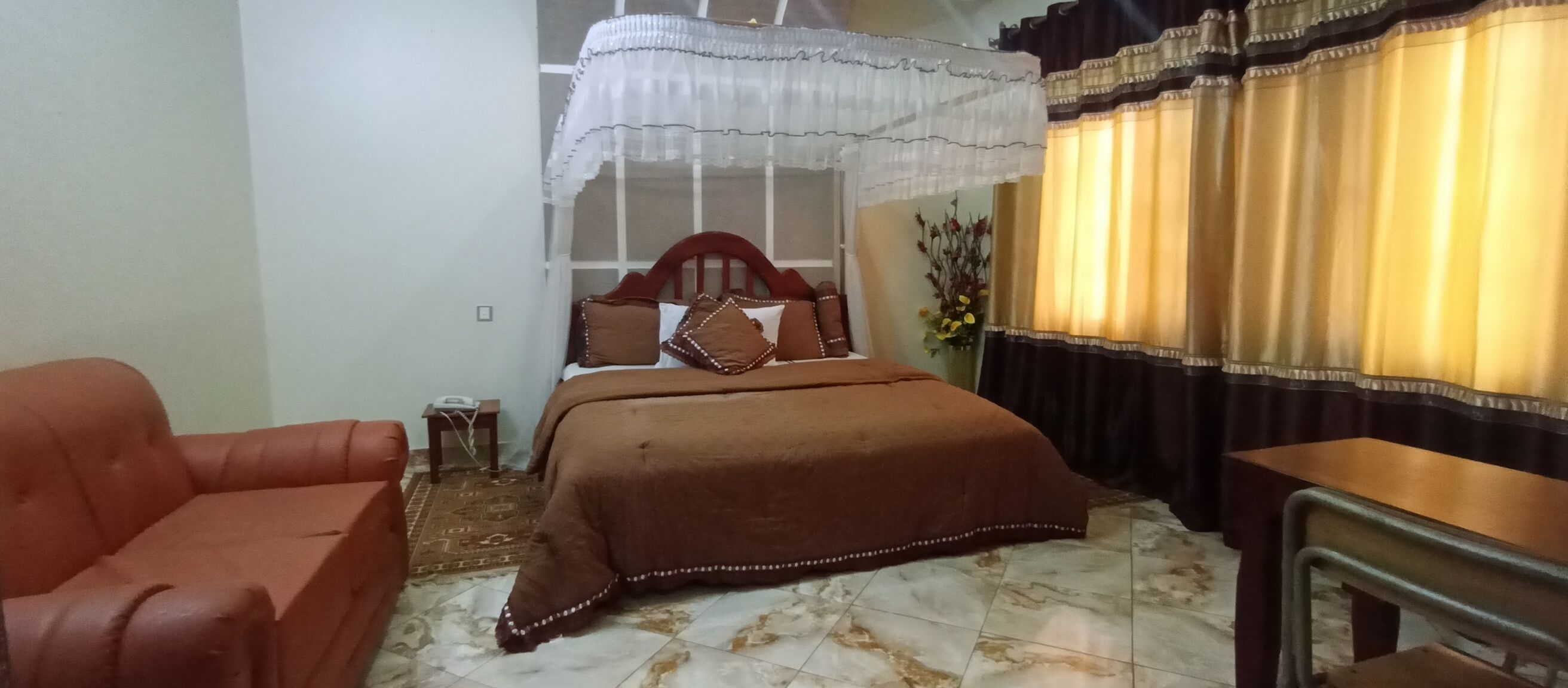 A bedroom with a bed, a chair, a small table, and a curtain.