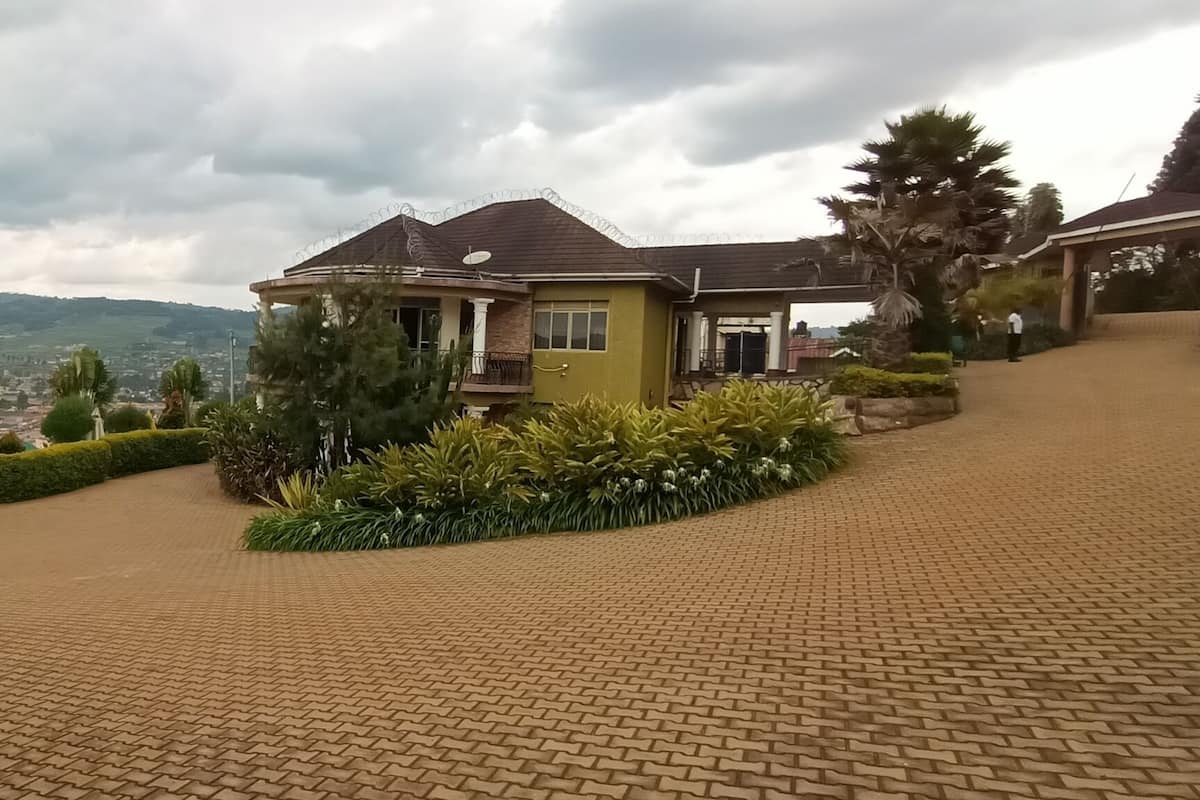 A house with a paved driveway, surrounded by greenery and a view of distant hills.