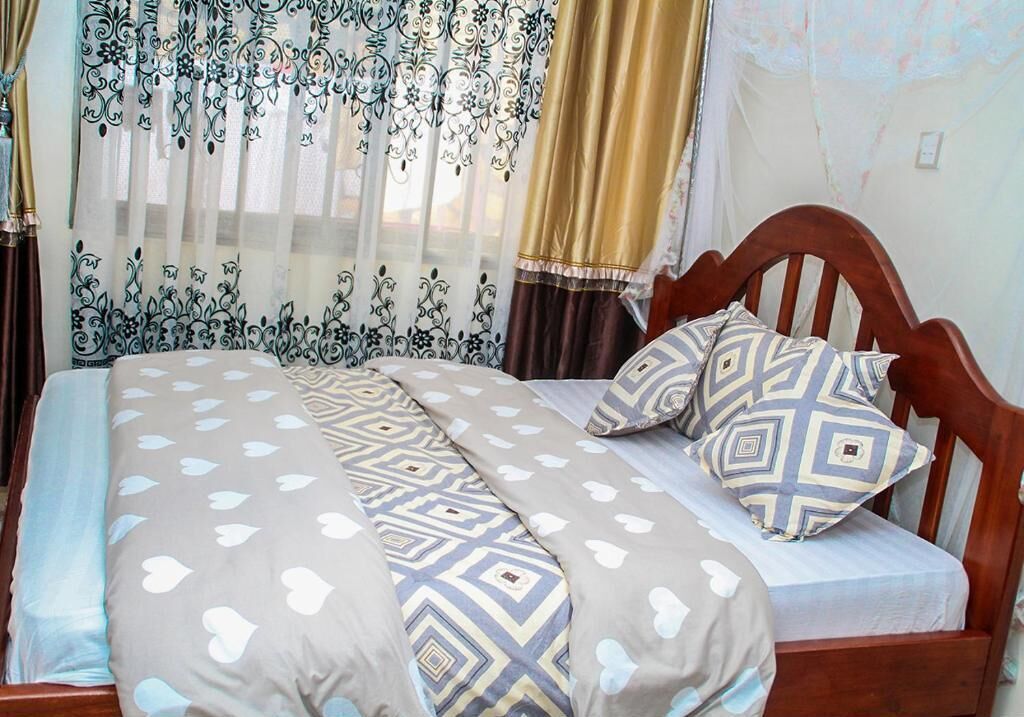 A bed with patterned bedding and pillows, curtains with a floral design, and a wooden headboard.