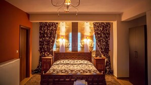 A bedroom with a large bed, two bedside tables, a chandelier, and patterned curtains.