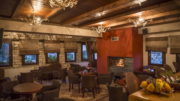 A cozy restaurant with stone walls, wooden beams, and a fireplace. There are multiple tables and chairs for dining.