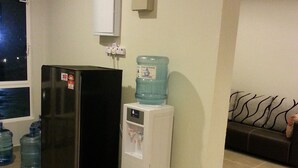 Uma cozinha compacta com geladeira, dispenser de água e relógio na parede.