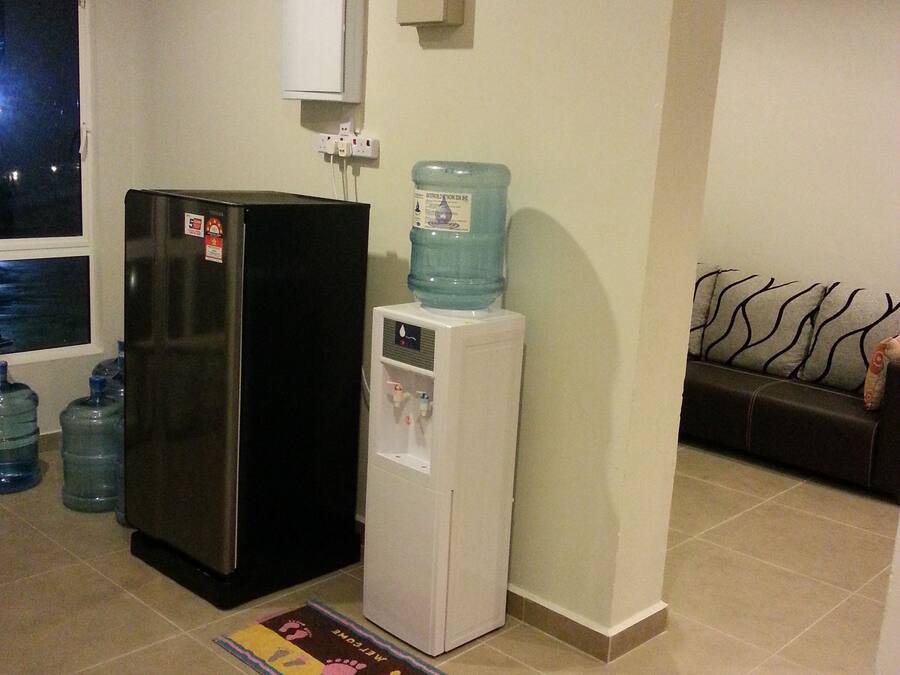 Cocina compacta con refrigerador, dispensador de agua y un reloj en la pared.