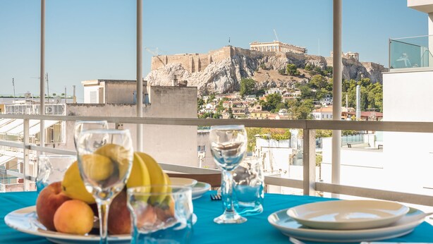 Una mesa con fruta y vasos, con vistas a un sitio histórico con ruinas y un paisaje urbano moderno.