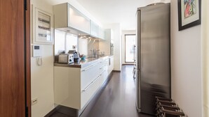 Una cocina moderna con electrodomésticos de acero inoxidable, horno empotrado y microondas. Se observa una puerta de madera a la izquierda y un refrigerador a la derecha.