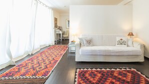 Una sala de estar con un sofá blanco, alfombras estampadas y una cortina blanca.