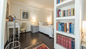 Una habitación de hotel con una cama, mesitas de noche, una estantería, una silla y un carrito.